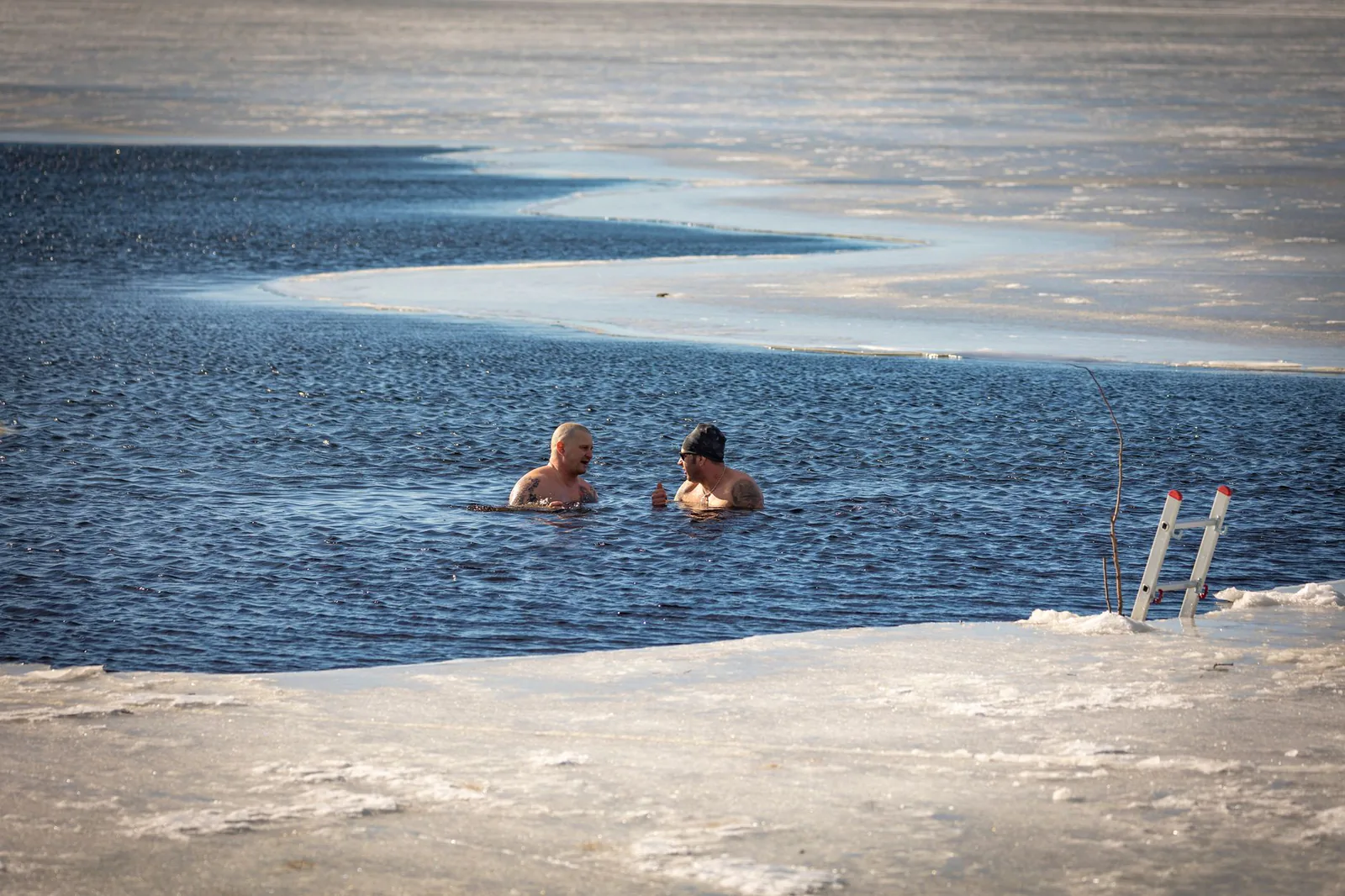 Two men cold plunging in a frozen lake